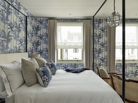 Sash window with wave curtains and sheer roman blinds in Old World bedroom. The room is decorated with blue palm tree wallpapers.
