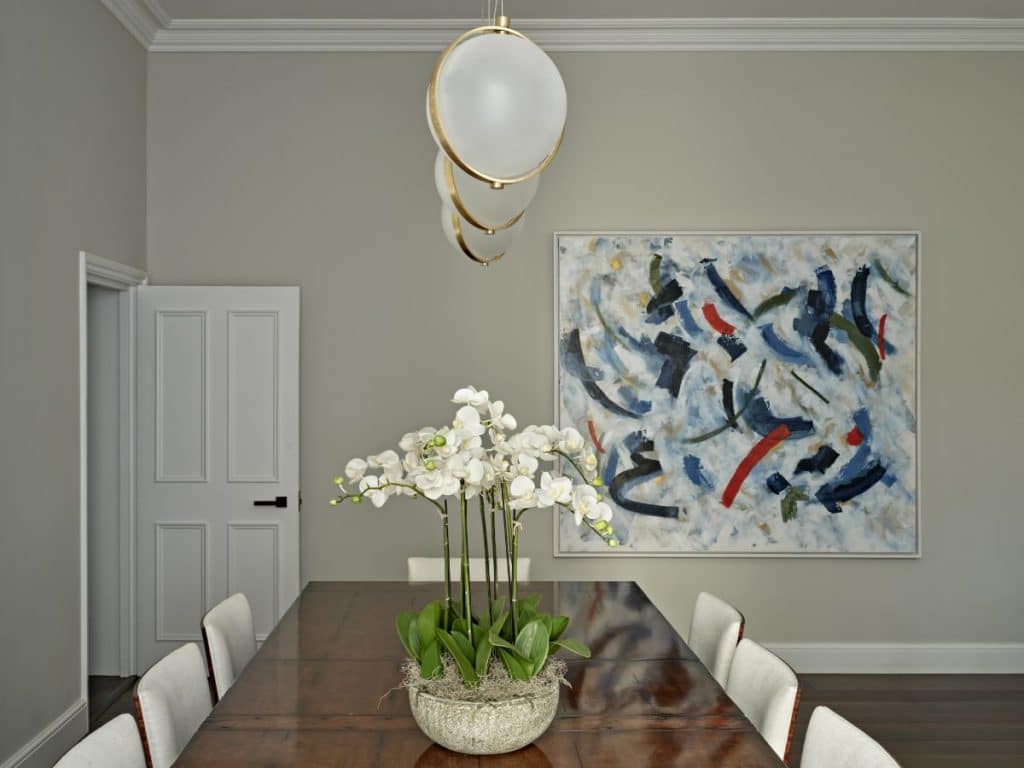 Dining room with baroncelli brass pendant lights and large oil painting on wall.