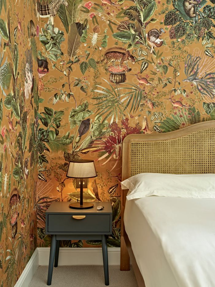 Extinct animal wallpaper by Moooi in a bedroom with blue bedside tables.