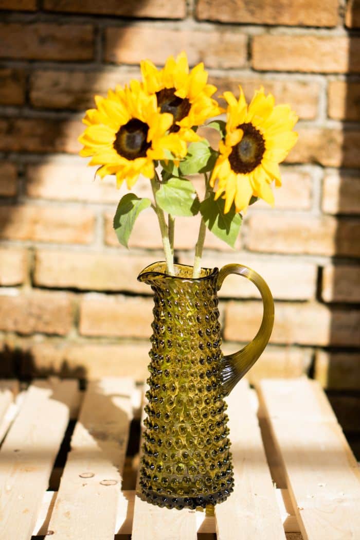 Bonsai green coloured hobnail glass jug with sunflowers in it. 