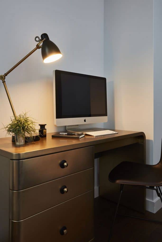 A modern brass desk creates a study area in the corner of a bedroom.