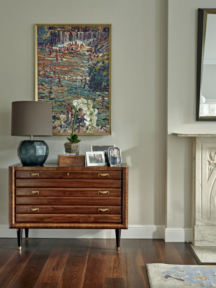 Beautiful wooden side cabinet in living room with lamp and art hanging above.