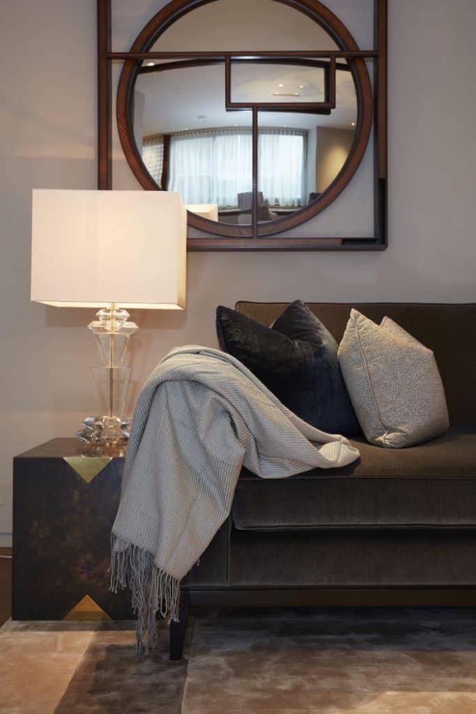 A corner of the living room showing a soft throw, mirror, side table and a lamp.