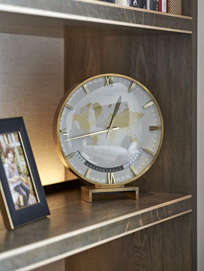 A zoomed-in image showcasing a personal arrangement of accessories on a bespoke dark wood joinery shelf. A majestic gold clock, with a captivating world map, adorned next to it, a cherished framed picture of a beloved young family member. This curated display creates sentimental charm and adds a touch of personalization.