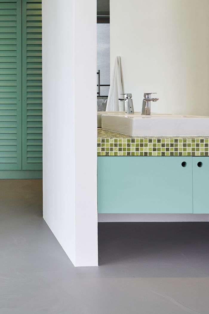 Teal green wardrobes and vanity storage in a walk in wardobe and bathroom with resin flooring. 