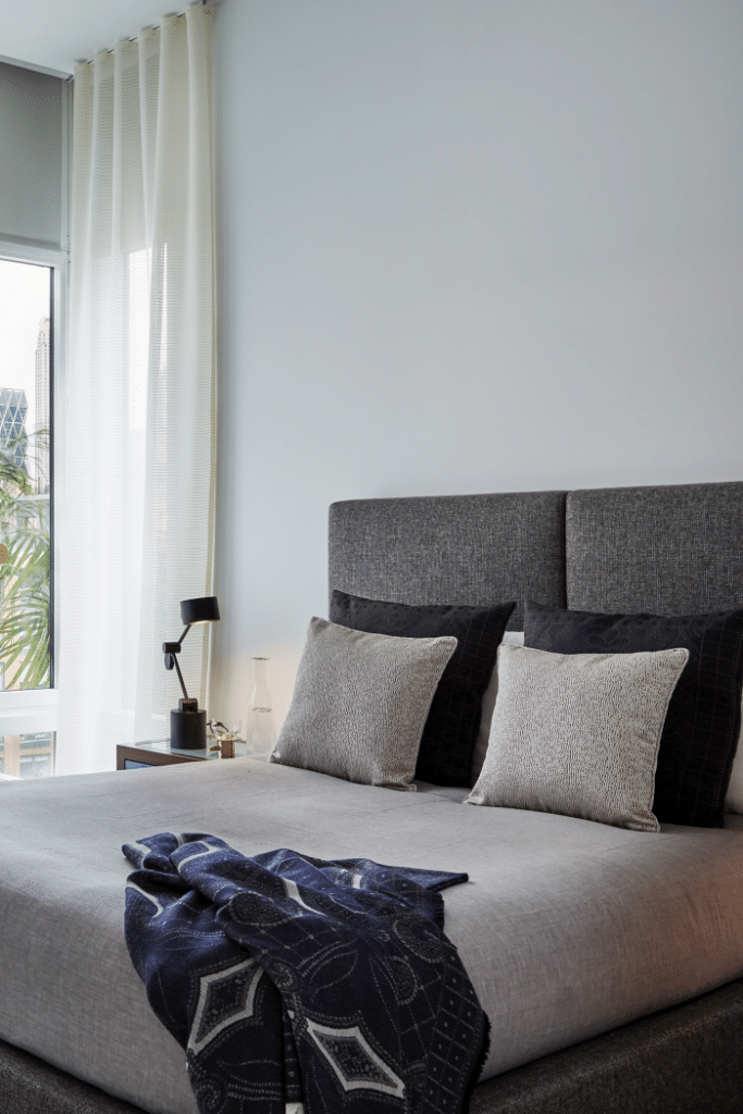 Crisp white bedroom furnished with blue and grey fabric headboard, throws and pillows.