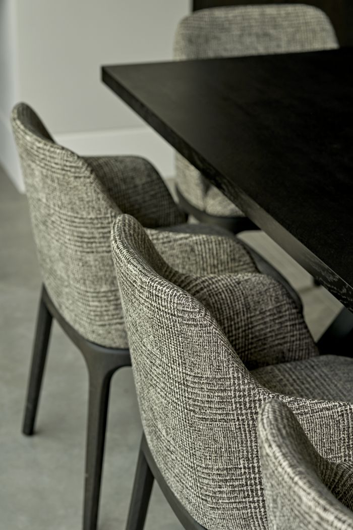 Up close image of grey patterned dining chairs with black legs, elegantly sitting around a Tom Faulkner dining table, adorned upon a complementary stone tile flooring.