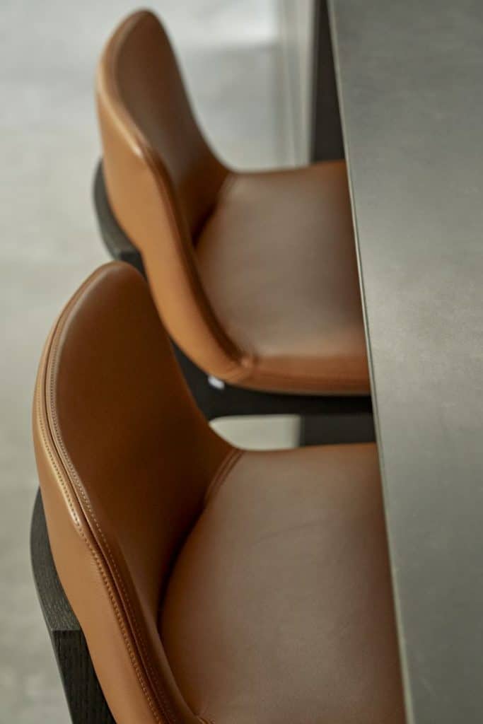 Up close image of a luxury brown leather bar stool with elegant dark wood legs, pushed up against a stone grey countertop.