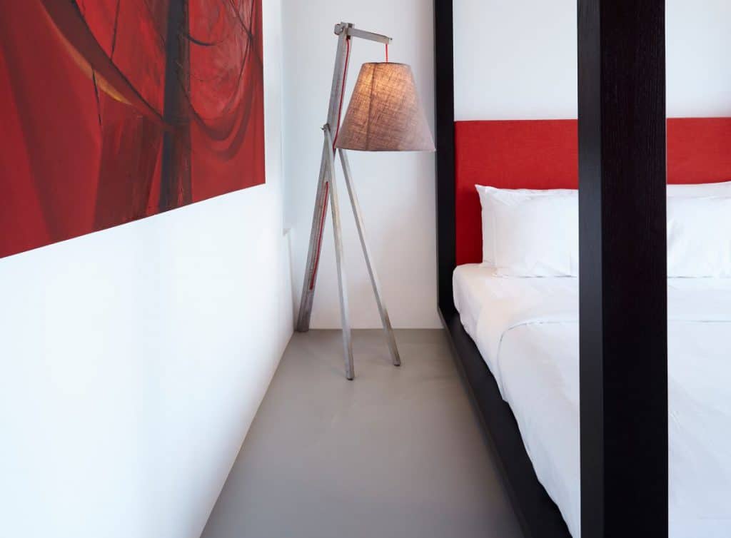 A black and red themed bedroom in a tropical villas with crisp white walls and grey resin flooring.
