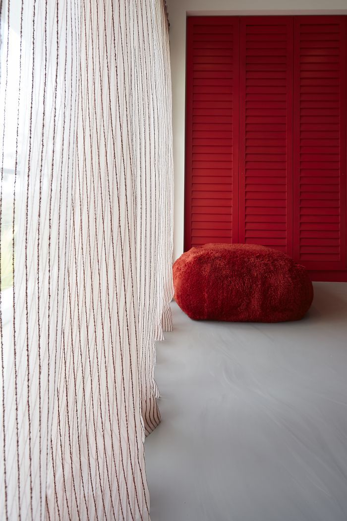 Pops of red featuring in sheer curtains and a fluff pouf pick up on the vibrant red coloured wardrobes in a bedroom.