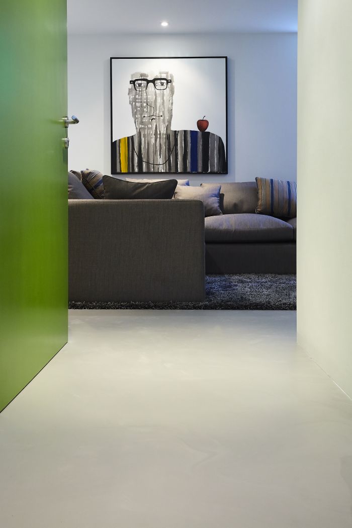 A grey seamless resin floor leads you from a hallway into the media room of this home. 