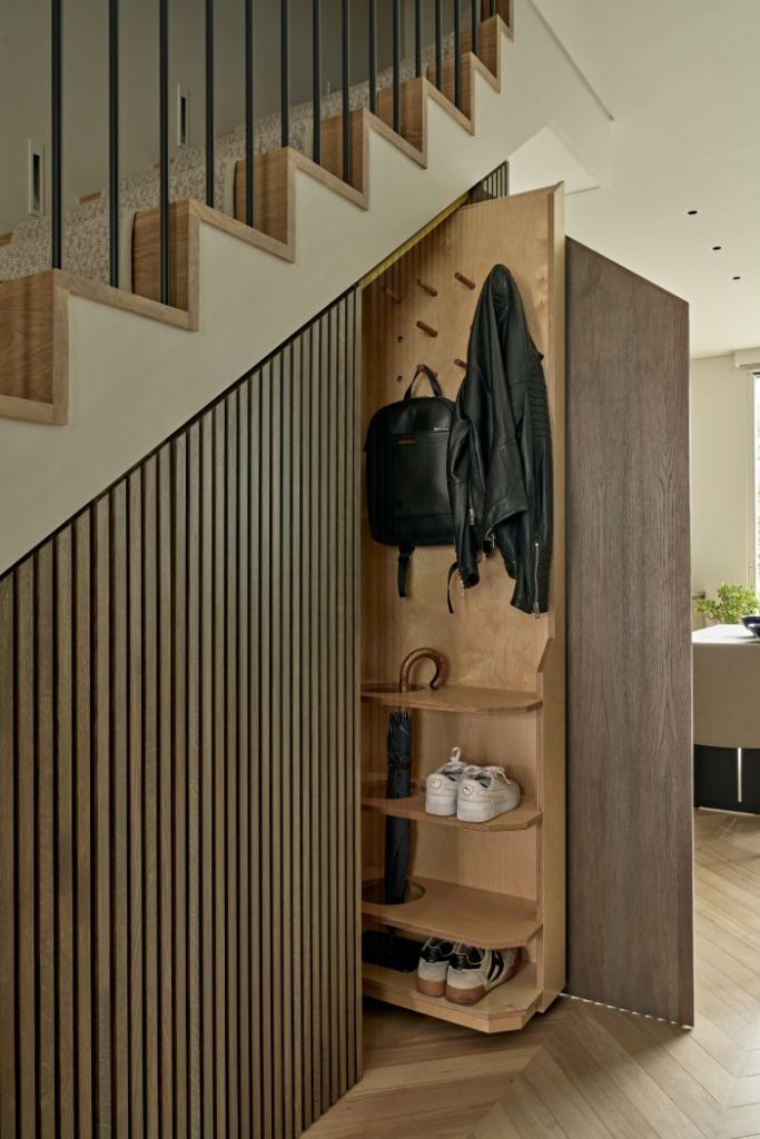 This luxurious under stairs showcases smart and efficient use of space. The slim paneled under stairs joinery features a pull-out storage unit, providing a practical solution for storing shoes, jackets, and bags. The light wood herringbone flooring harmonises with the light wood stairs, creating a cohesive and visually appealing look. A cream carpet running upstairs adds a touch of warmth and elegance. This cleverly designed under stairs room maximises functionality while maintaining a stylish and sophisticated atmosphere.