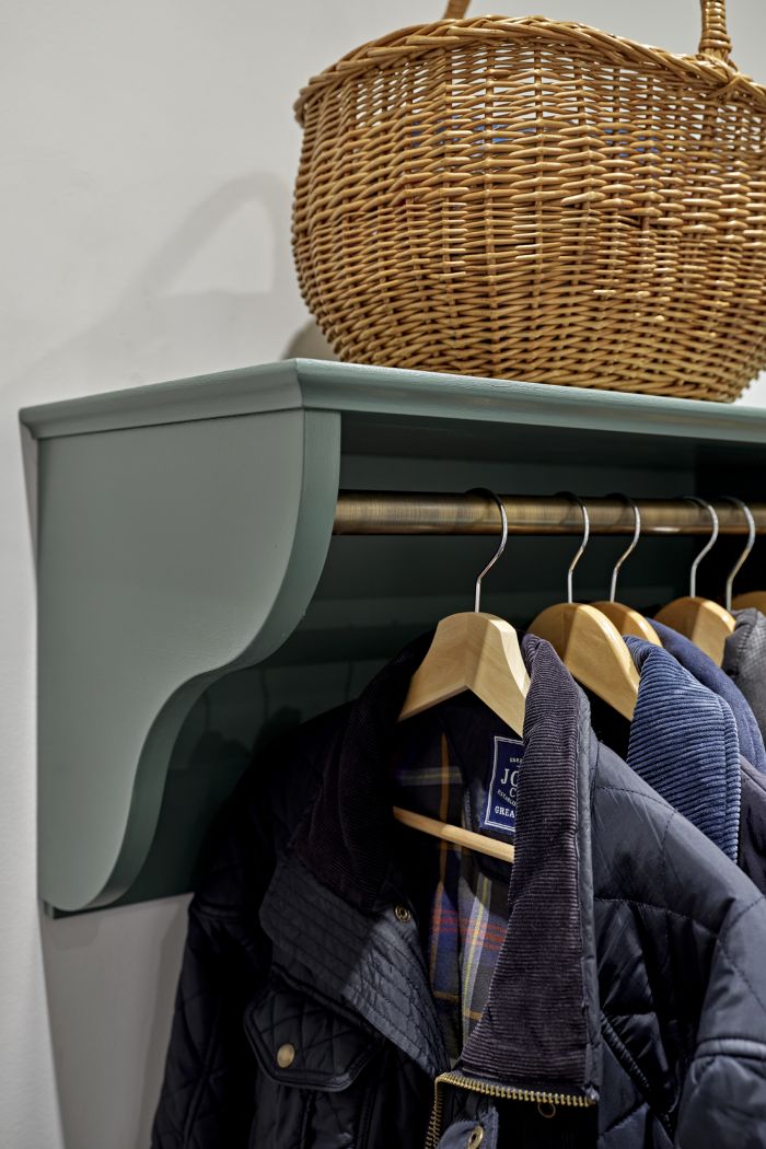 Up close image of jackets hanging on a bronze rail supported by a blue shelf , with a carefully positioned wicker basket resting on top.