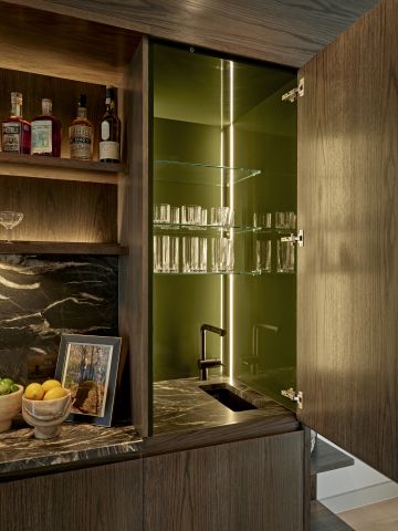 An elegant moody home bar in luxury London home. The countertop is a beautiful dark marble and the cabinets and shelves are dark toned wood.
