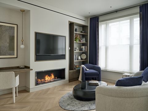 A luxury living room with a modern fireplace in the center with a tv above. Neutrals and navy colours are dominating.