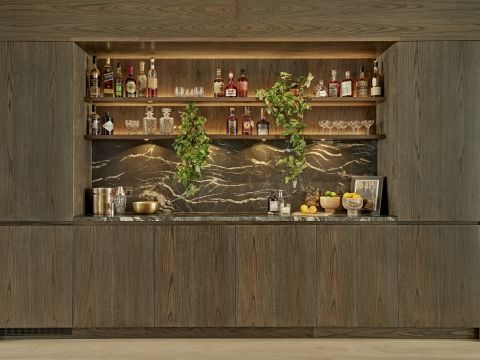 A luxury bespoke home bar in an entertaining area with stained wood and black marble.