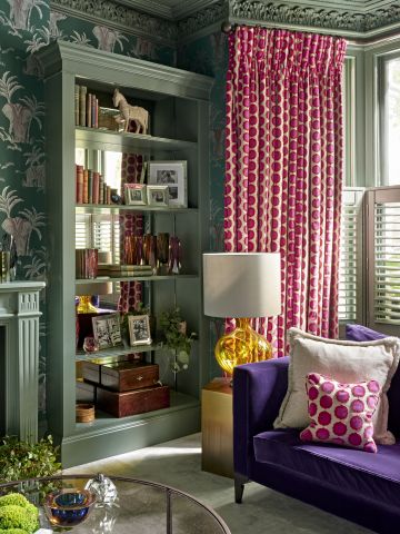 Green living room with pops of colour in furniture and curtains. The vibrant colours in the room are purple, magenta, and shades or greens.