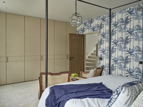 Old World-styled guest bedroom. The primary colours in the bedroom are blue tones and neutral tones. The statement wallpaper is filled with blue palm tree design.