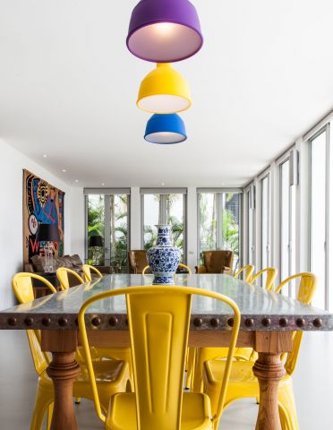 A bright yellow coloured set of dining chairs around a zinc topped dining table in a tropical villa.