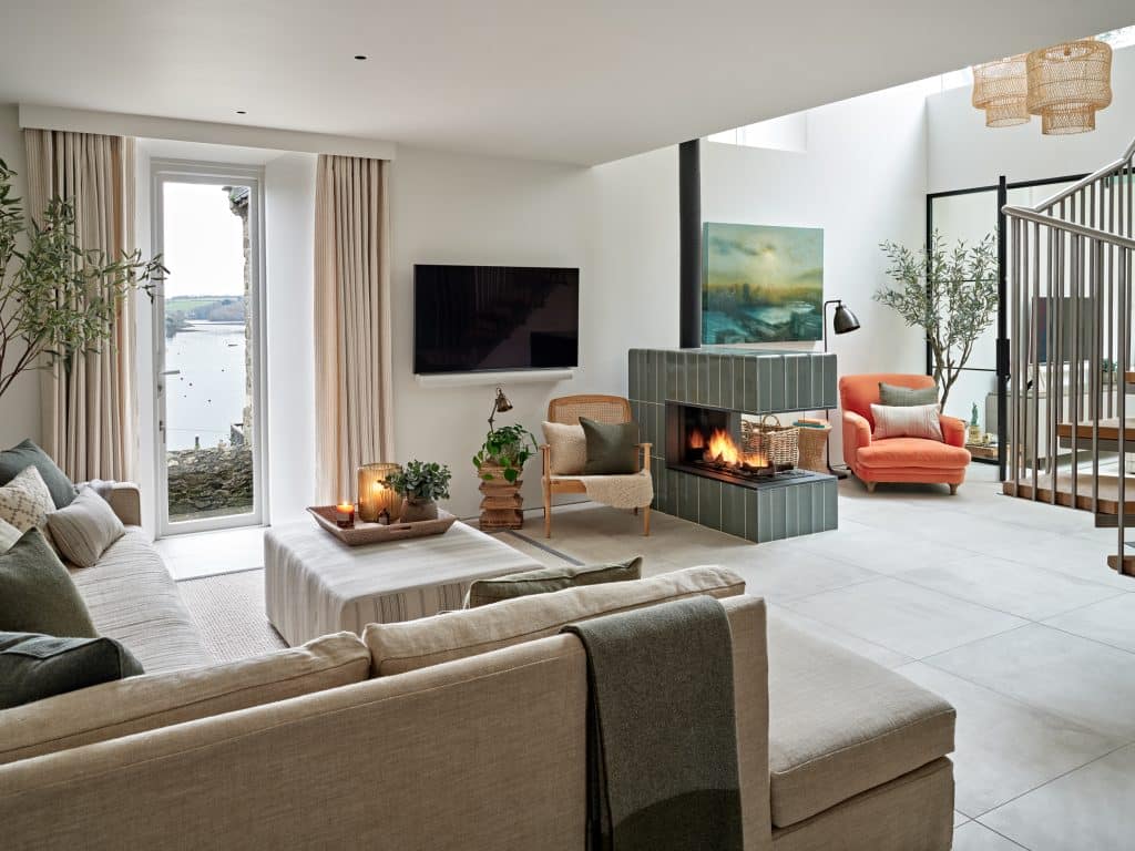 Neutral living space with green tiled fireplace which separates the living space from the reading nook in coastal style house.