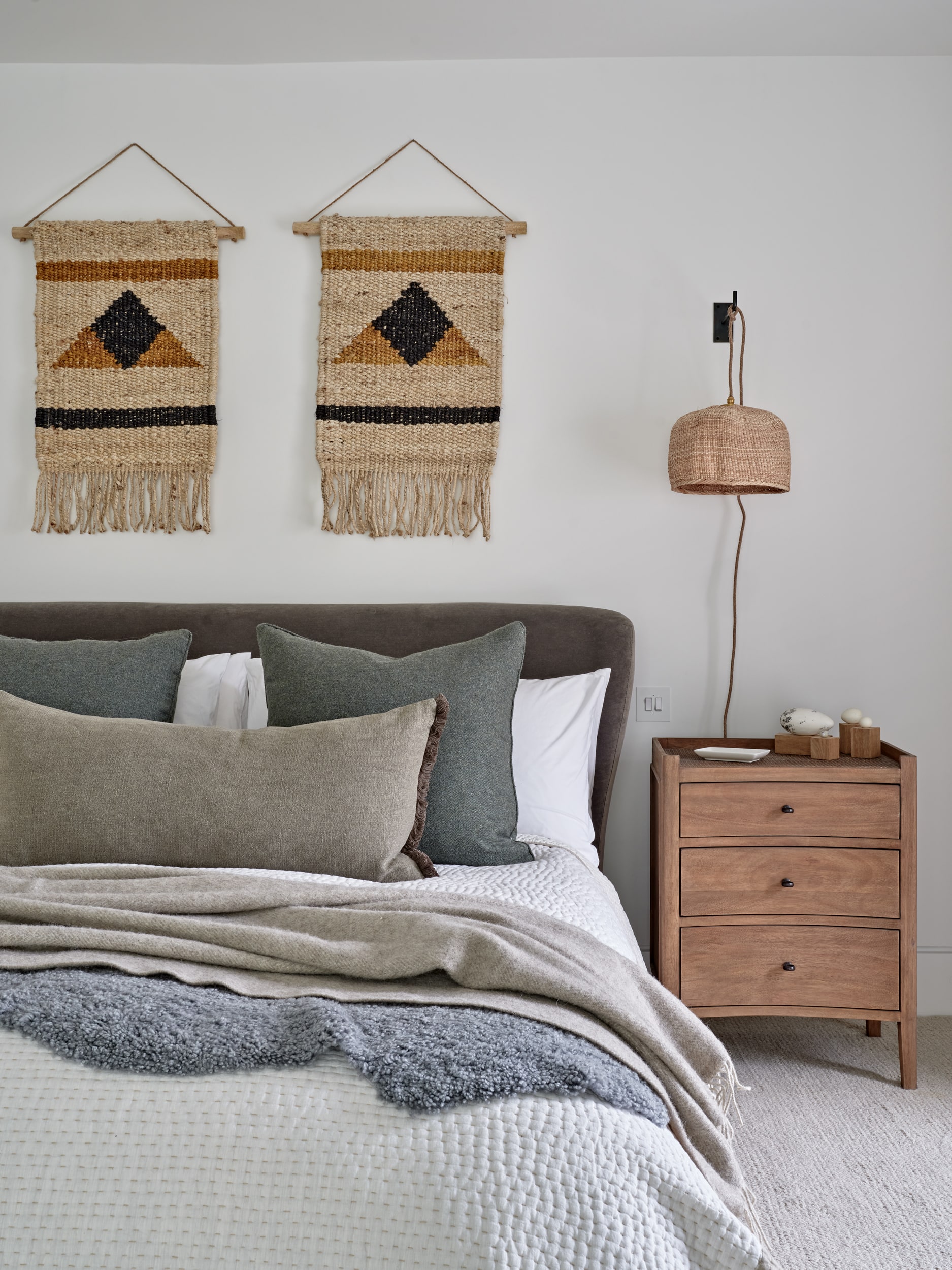 Brown wood bedside table with rattan pendant light above in coastal style bedroom.