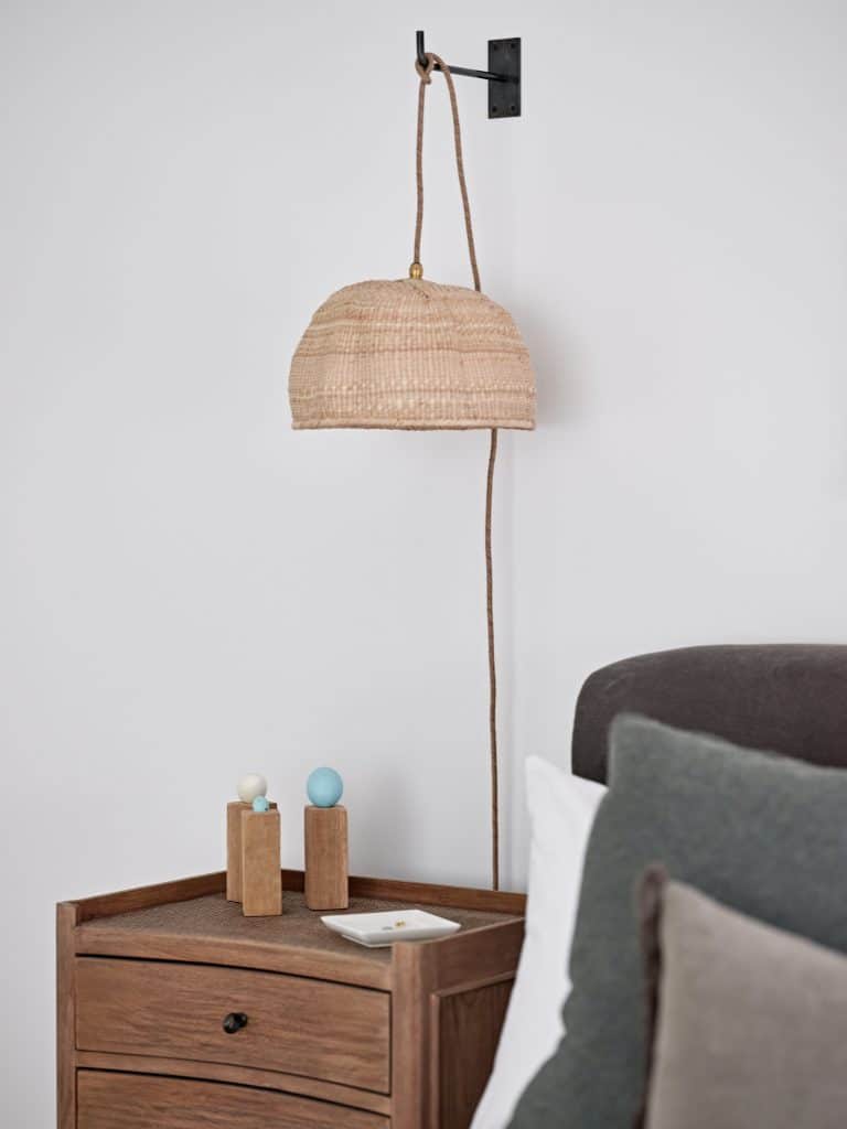Rattan pendant light above wooden bedside table.