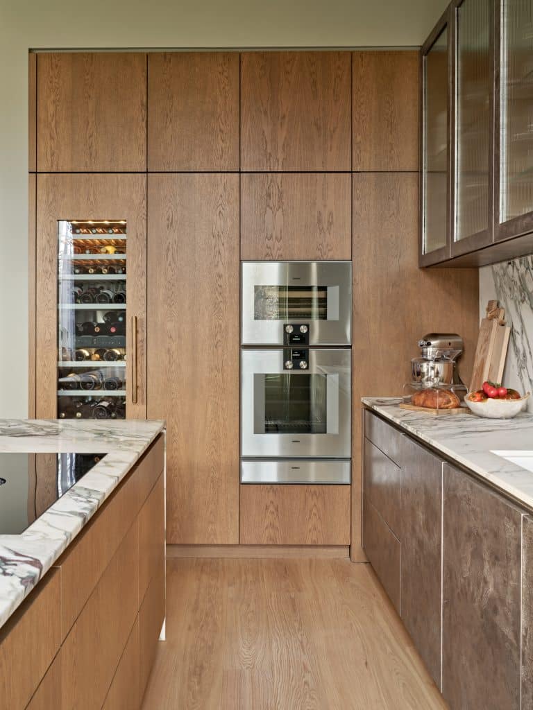 Bespoke wooden cabinets in mid century modern kitchen. The warm tone of the wood and the marble counter top create a great contrast between materials and colours. In the built in cabinets there is a build in wine fridge, and steam and regular ovens.