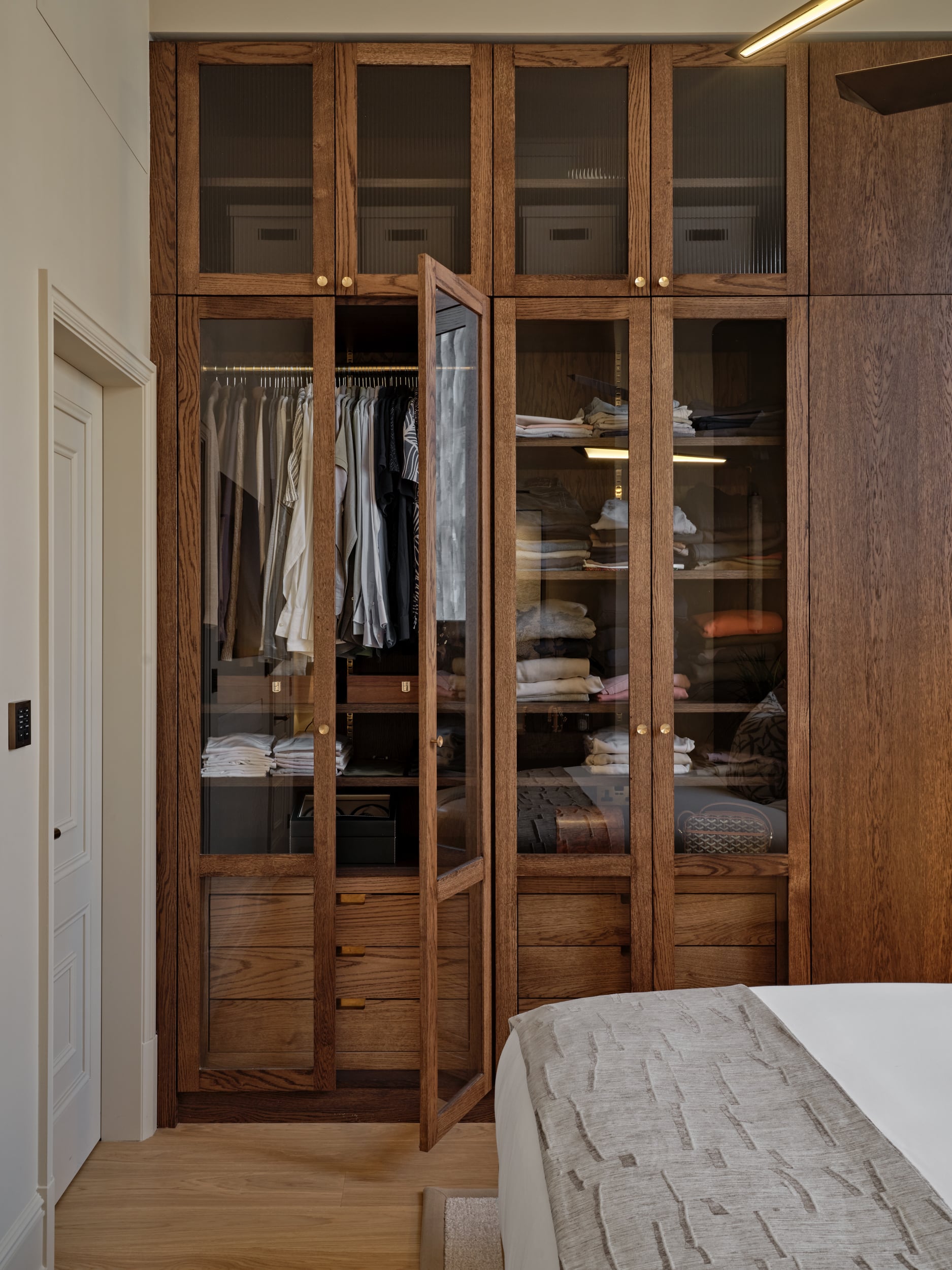 A bespoke wardrobe in a bedroom, making optimum use of space and keeping things sleek. The design appeals both aesthetically and functionally, accommodating the existing clothing, shoes, accessories, and so on, while also leaving enough room for new purchases. The custom wardrobe in the bedroom allows the owner to stay organised and enjoy getting ready in the mornings.